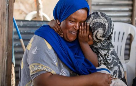 Qadan pictured wearing blue smiles as one of her children whispers in her ear